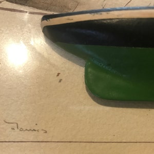 May include: Close-up of a green, black and white model ship hull. The ship is painted with a green bottom, black midsection and white top. The ship is signed "Tommis".