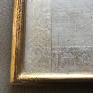 May include: Close-up of a gold-colored frame with a textured surface. The frame is made of wood and has a slightly distressed look.