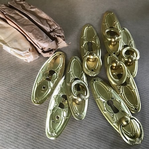 May include: A set of eight gold-toned oval cabinet door pulls with keyhole cutouts and decorative rings.