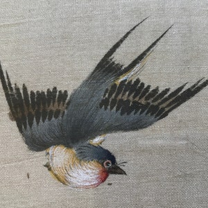 May include: A painted image of a brown and gray bird with black wings flying in mid-air. The bird is painted on a beige linen background.