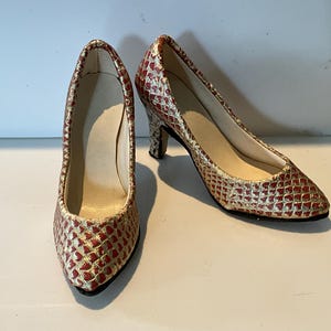 May include: A pair of red and gold patterned court shoes with a pointed toe and a small heel. The shoes have a snakeskin-like texture and a neutral-colored interior. The shoes are displayed on a white surface.