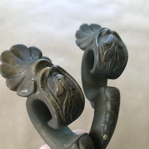May include: Close-up of two antique bronze-colored drawer pulls. Each pull features a decorative floral design with a curved handle. The pulls are likely vintage or antique, adding a touch of elegance to furniture.