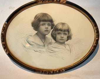 May include: A framed black and white portrait of two young girls with short hair. The girls are wearing light-coloured dresses and are looking at the viewer. The frame is oval-shaped with a gold-coloured trim.