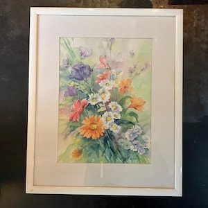 May include: A framed watercolor painting of a bouquet of colorful flowers, including purple, orange, yellow, and white flowers. The flowers are arranged in a vase and are surrounded by green leaves. The painting is signed "M.E. Brown" in the bottom right corner.