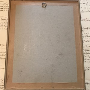 May include: A wooden frame with a light brown mount and a brass hanging ring. The frame is empty and has a light brown wood finish. The frame is surrounded by a white background.