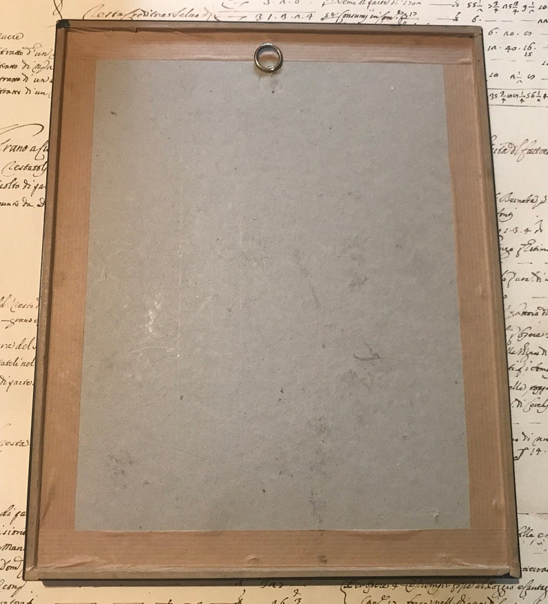 May include: A wooden frame with a light brown mount and a brass hanging ring. The frame is empty and has a light brown wood finish. The frame is surrounded by a white background.