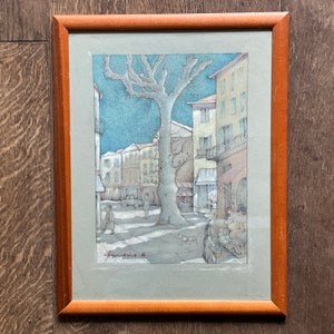 May include: A framed watercolor painting depicting a street scene in a European town. The painting features a large tree in the center, with buildings on either side. The buildings are painted in shades of gray and brown, and the tree is painted in shades of green and brown. The painting is signed in the lower right corner.