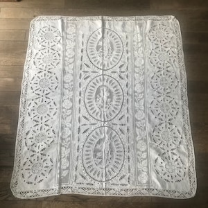 Peut inclure: Nappe en dentelle blanche avec un motif floral délicat et des motifs circulaires complexes. La nappe est faite d'un matériau fin et léger et a une touche délicate et féminine.