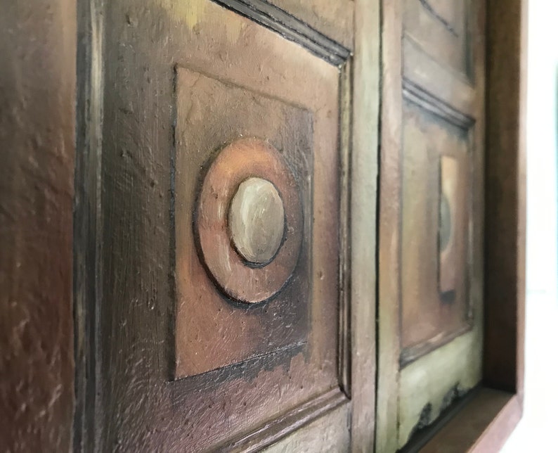 Op de afbeelding: Een close-up van een houten wandkunstwerk met een geometrisch ontwerp. Het stuk is geschilderd in tinten bruin, groen en wit. Het ontwerp bevat een reeks vierkanten en cirkels.