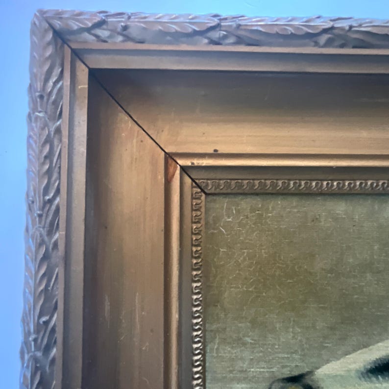 May include: Close-up of a vintage painting in a gold-colored wooden frame. The frame has a detailed, ornate design with a textured surface. The painting's colors are muted, with visible brushstrokes.