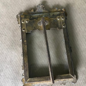 May include: A gold-toned metal picture frame with an ornate design. The frame has a glass front and a metal stand on the back. The back of the frame has the inscription "W.H. MILLER & CO."