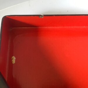 May include: The inside of a red lacquered box with a black rim. The box has a small white mark on the inside.