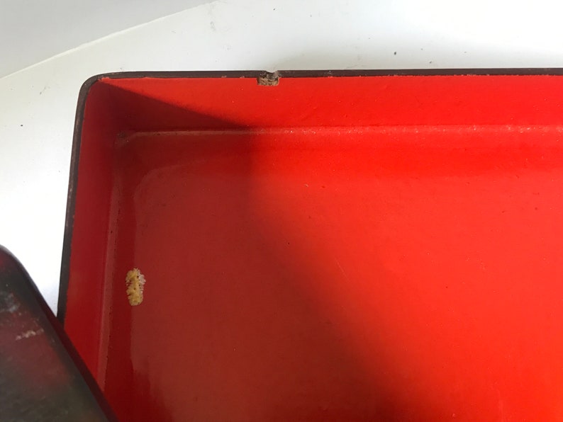 May include: The inside of a red lacquered box with a black rim. The box has a small white mark on the inside.
