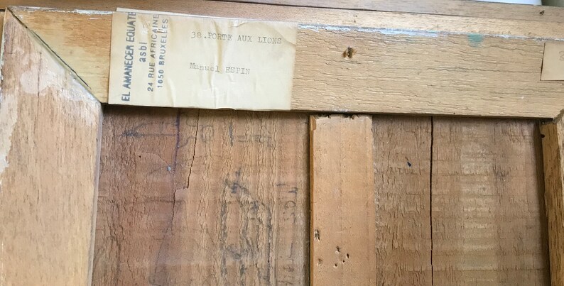 Op de afbeelding: Een close-up van een houten frame met een label eraan bevestigd. Het label luidt "EL AMANECER EQUATE asbl 24 RUE AFRICAINE 1050 BRUXELLES 38-PORTE AUX LICONS".