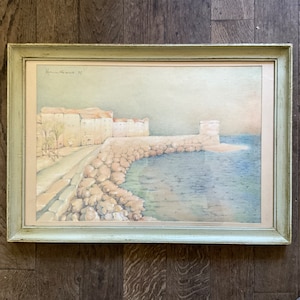 May include: A framed watercolor painting of a coastal town with a stone wall and a body of water. The painting is signed "Handrose 31" in the top left corner.