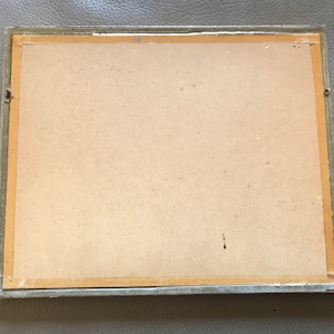 May include: A plain, off-white picture frame with a light brown mat and a silver-colored frame. The frame is slightly damaged on the top left corner.
