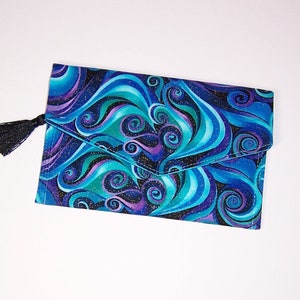 May include: A blue and purple fabric clutch with a black tassel. The fabric has a swirling pattern with glitter accents.