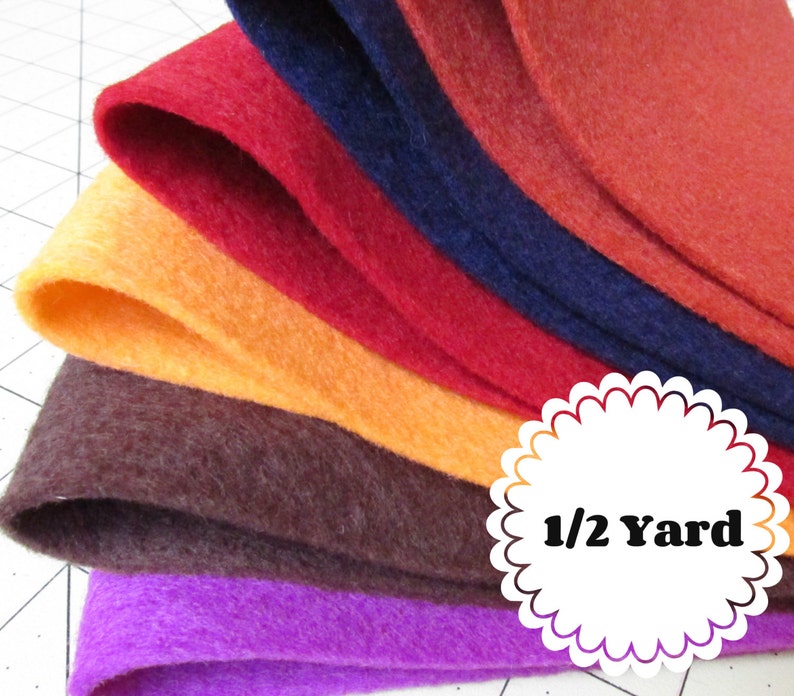 May include: A stack of six felt fabric squares in various colors, including purple, brown, orange, red, dark blue, and rust. The fabric is folded in half and the top layer is slightly curled. A white circle with a black border and the text "1/2 Yard" is in the lower right corner of the image.