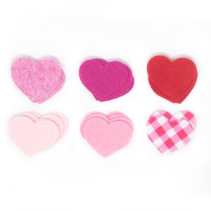 May include: Six felt hearts in various shades of pink and red. The hearts are layered on top of each other, creating a dimensional effect. One heart has a gingham pattern.