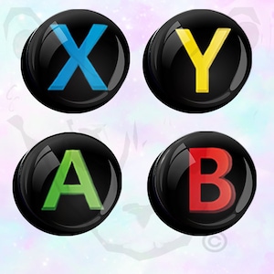 Puede incluir: Cuatro botones negros con un acabado brillante, cada uno con una letra de color diferente. Las letras son X en azul, Y en amarillo, A en verde y B en rojo.