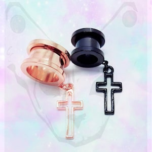 May include: Two pairs of ear gauges with dangling cross charms. One pair is rose gold and the other is black.