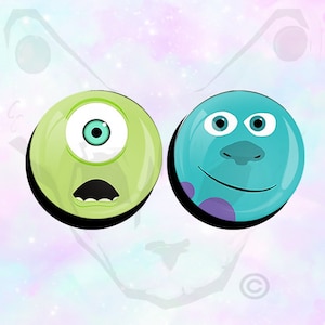May include: Two round buttons with cartoon faces. The button on the left is green with one large blue eye and a surprised expression. The button on the right is blue with two white eyes and a purple spot.