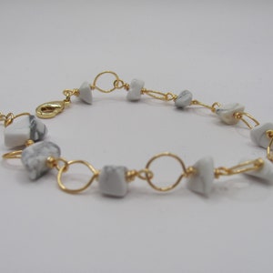 May include: A gold chain bracelet with white and gray stone beads. The bracelet has a clasp closure.
