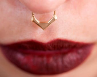 May include: Close-up of a person's face with a gold septum ring and a silver nose ring. The person is wearing dark red lipstick.