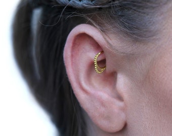 May include: A close-up of a person's ear with a gold hoop earring in the helix piercing.