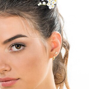 May include: A close-up of a woman's ear with two gold leaf earrings. The earrings are small and delicate, and they are a popular choice for women who want a subtle and stylish look.