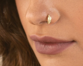 May include: A gold nose ring with a textured design. The ring is in the shape of a crescent moon.