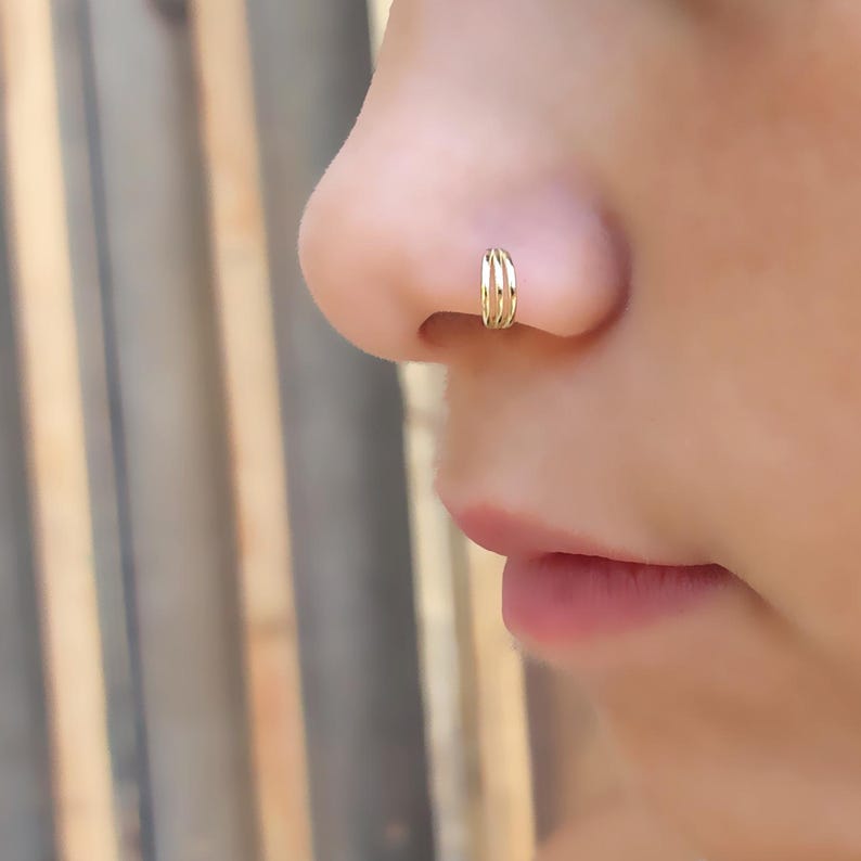 May include: Gold nose ring with three thin bands. The ring is worn in the left nostril.