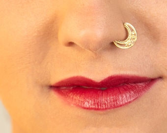 May include: A close-up of a person's face with a gold crescent moon nose ring. The person is wearing red lipstick.