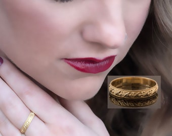 May include: A gold wedding band with a delicate floral design. The band is shown on a finger and in a close-up view.