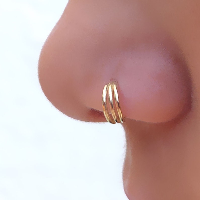 May include: A gold nose ring with three stacked hoops.