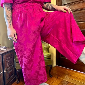 May include: A bright pink wide-leg pantsuit with a floral pattern. The pants have an elastic waistband and the top has short sleeves.