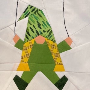 Peut inclure: Un gnome en patchwork vert et jaune tenant des ballons verts. Le gnome porte un chapeau vert avec un motif blanc et vert.