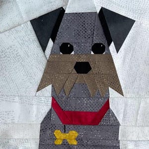 May include: A fabric quilt block featuring a stylized gray dog with a speckled pattern, black ears, and a tan muzzle. The dog wears a bright red collar with a yellow bone-shaped tag. The entire figure is set against a white background with a subtle texture.