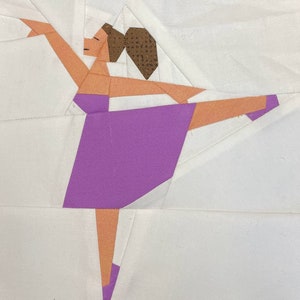 Puede incluir: Una pieza de arte textil que representa a una bailarina en una pose elegante. La bailarina tiene un maillot morado, brazos y piernas color melocotón y un moño marrón. El fondo es blanco, con formas y líneas geométricas.