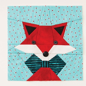 May include: A red fox face made from fabric scraps. The fox has black eyes, a white muzzle, and a blue and black bow tie. The background is a turquoise fabric with white polka dots.