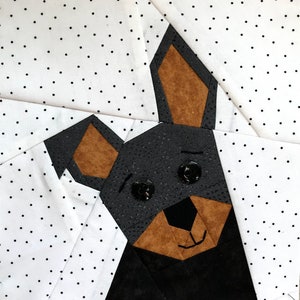 May include: A black and brown patchwork fabric dog with button eyes. The dog is made of different fabric pieces sewn together to create a geometric design.