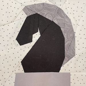 May include: A black and gray fabric horse head with a swirl pattern on the mane. The horse head is on a white background with black polka dots.