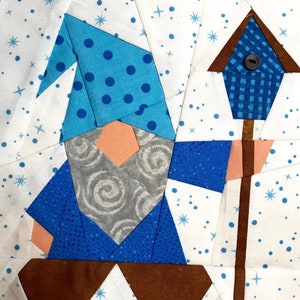 Peut inclure: Un gnome en patchwork bleu et marron tenant une maison d'oiseau bleue avec un toit marron et un bâton marron. Le gnome porte un chapeau bleu à pois blancs et une barbe grise avec un motif en spirale. L'arrière-plan est blanc avec des étoiles bleues.
