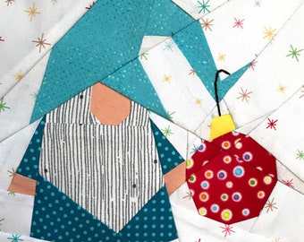 May include: A patchwork gnome holding a red and white polka dot ornament with a yellow top. The gnome is wearing a teal hat and a teal and white striped shirt. The background is white with a scattered pattern of colorful stars.