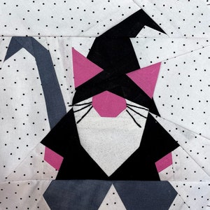 Op de afbeelding: Een zwarte en roze papier-geplakte kat met een tovenaarshoed. De kat heeft een witte baard en snorharen. De achtergrond is wit met zwarte stippen.