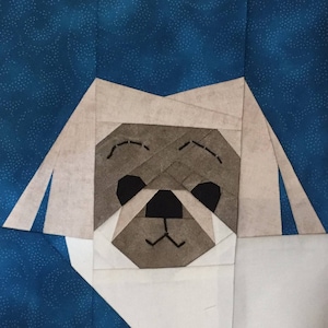 May include: A white fabric dog with a brown face and black eyes. The dog is made of fabric squares sewn together.