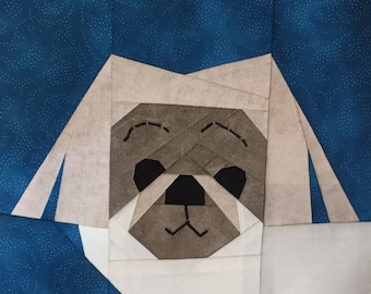 May include: A white fabric dog with a brown face and black eyes. The dog is made of fabric squares sewn together.