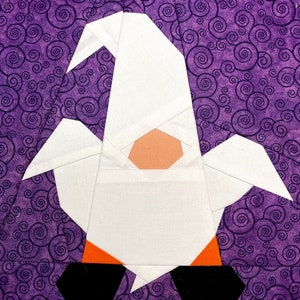 Puede incluir: Un gnomo de fieltro blanco con un sombrero naranja y botas negras. El gnomo está sentado sobre un fondo morado con un patrón de espiral.