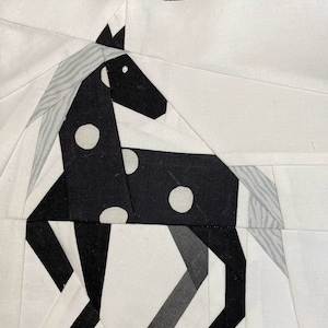 Peut inclure: Un cheval noir et blanc avec des pois blancs, fait de chutes de tissu. Le cheval est debout sur un fond blanc.