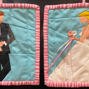 May include: Two quilted pot holders featuring a bride and groom. The bride is wearing a white dress with a pink sash and a bouquet of flowers. The groom is wearing a black suit with a white shirt and a black bow tie. Both pot holders have a pink and white striped border.